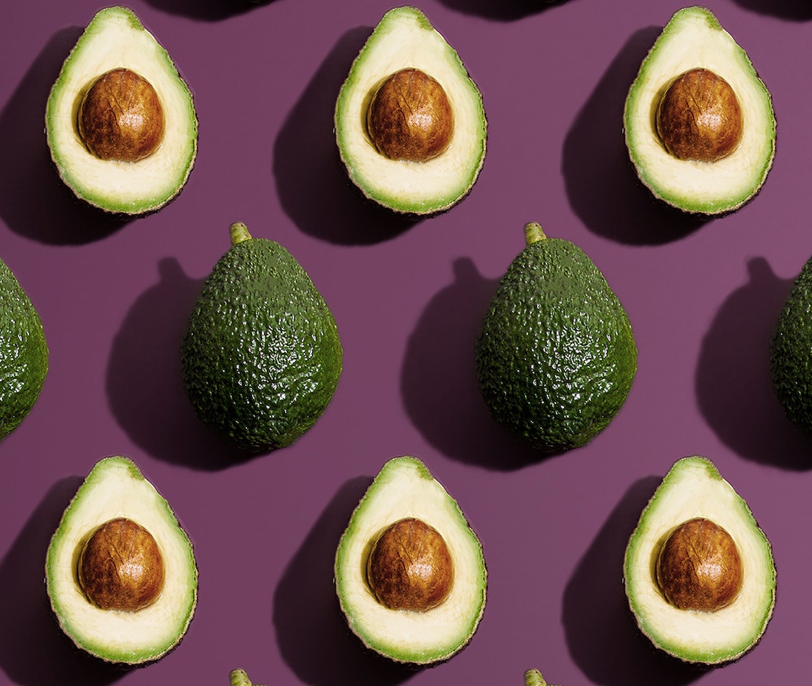 Pattern of whole and halved avocados on a purple background
